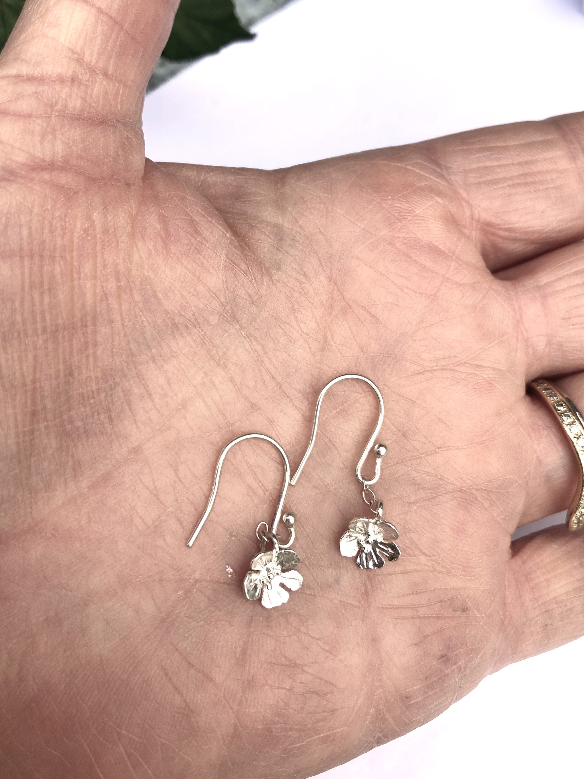 palm of hand holding two speedwell silver floral hook earrings