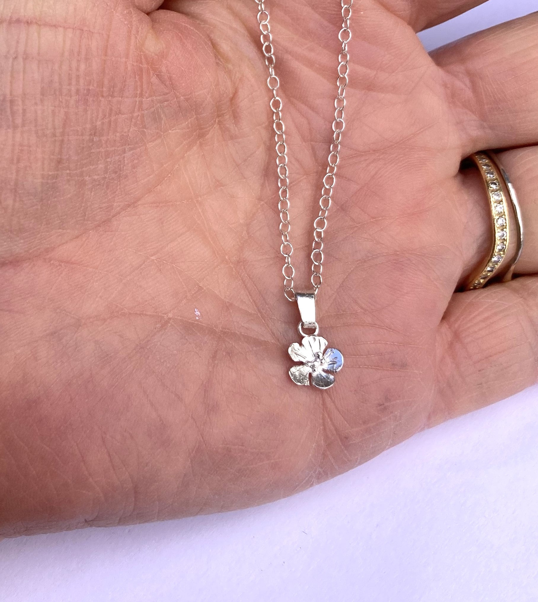 tiny silver single flower pendant and chain held in palm of hand