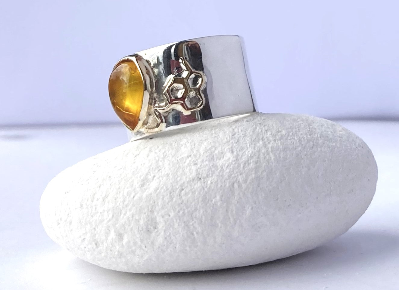 wide silver ring with whimsical gold honeycomb detail and amber drop, on white pebble