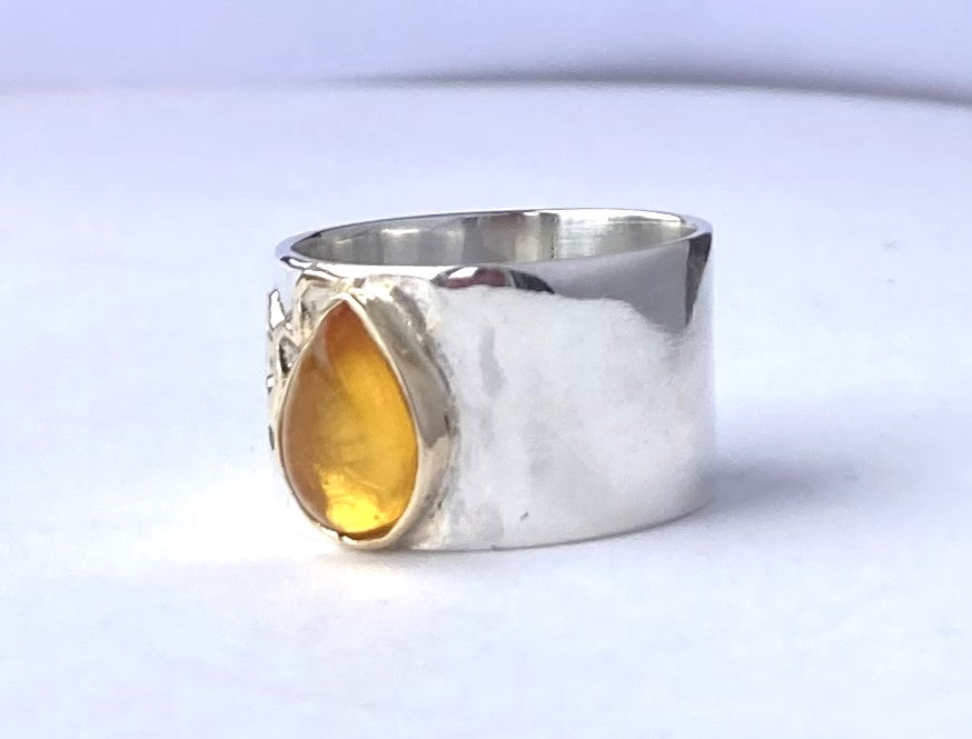 pear shape amber set on wide silver ring, on white background