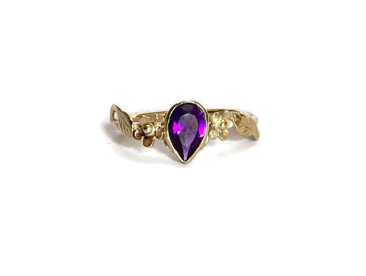 strong amethyst gemstone in pear shape set in gold floral ring, on white background