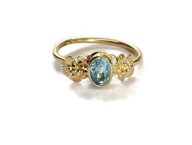 gold floral ring set with oval pale blue gemstone with flowers each side, on white background