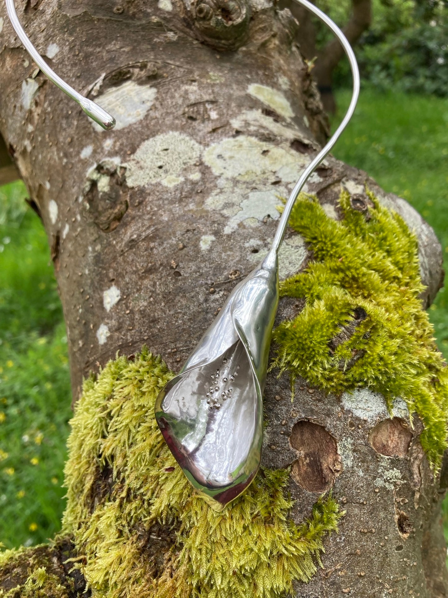 silver cala lily torque necklace on a mossy tree