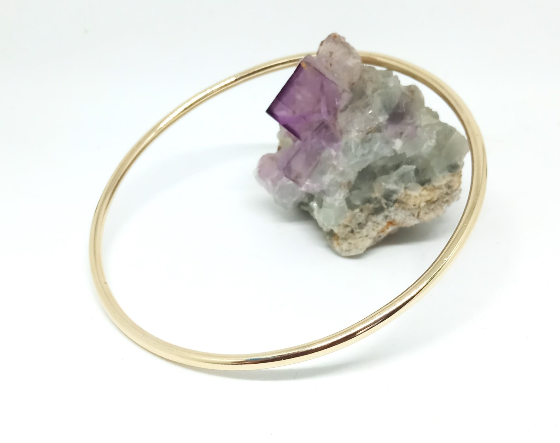  yellow 9ct gold circle bangle resting on amethyst crystal, unisex bracelet, on white background