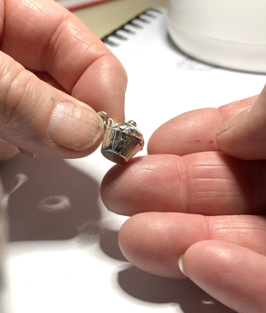 tiny silver cupcake pendant held in fingers