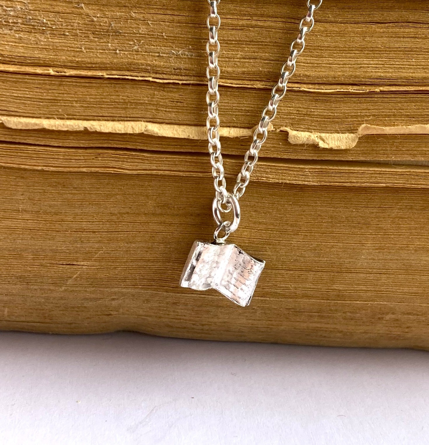 tiny silver book pendant on old book