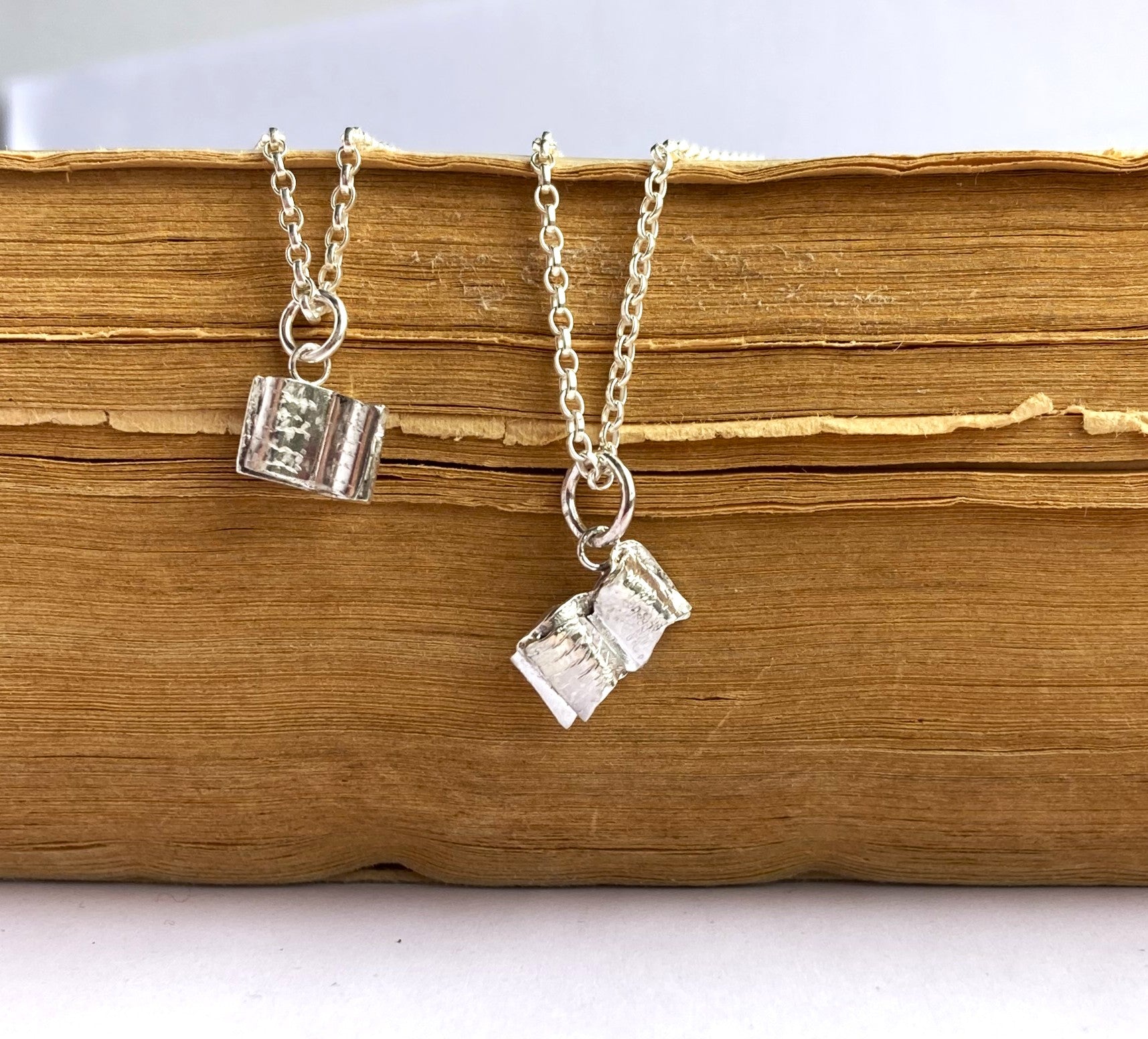 miniature hand made silver book pendants on old brown book pages