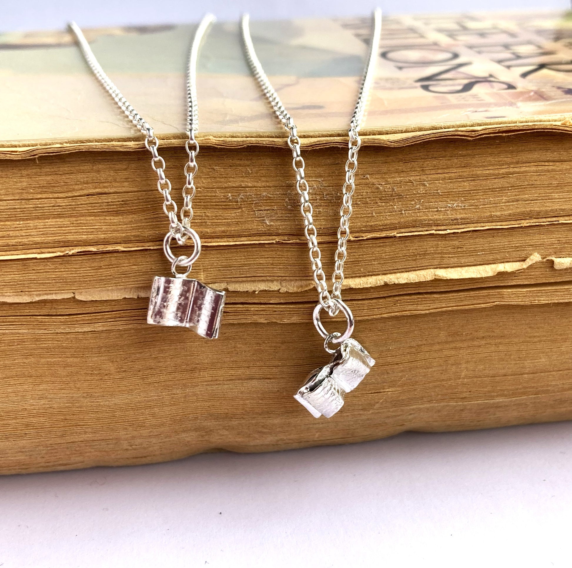 two small silver book theme pendants on an old book