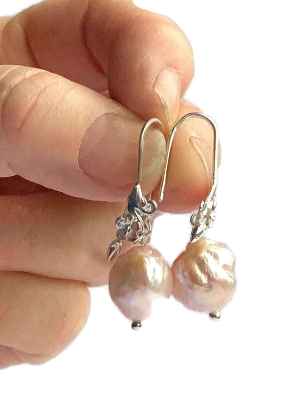 pink baroque pearl drop earrings held in fingers