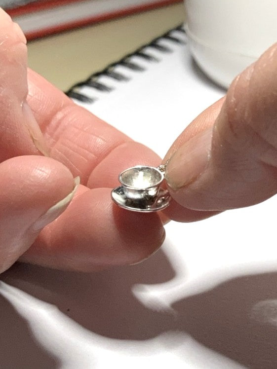 tiny silver  teacup pendant held in fingers