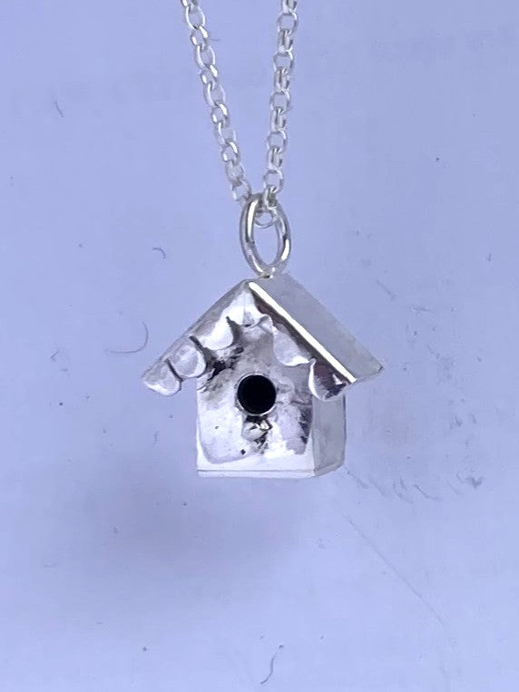 miniature silver birdhouse pendant on grey background