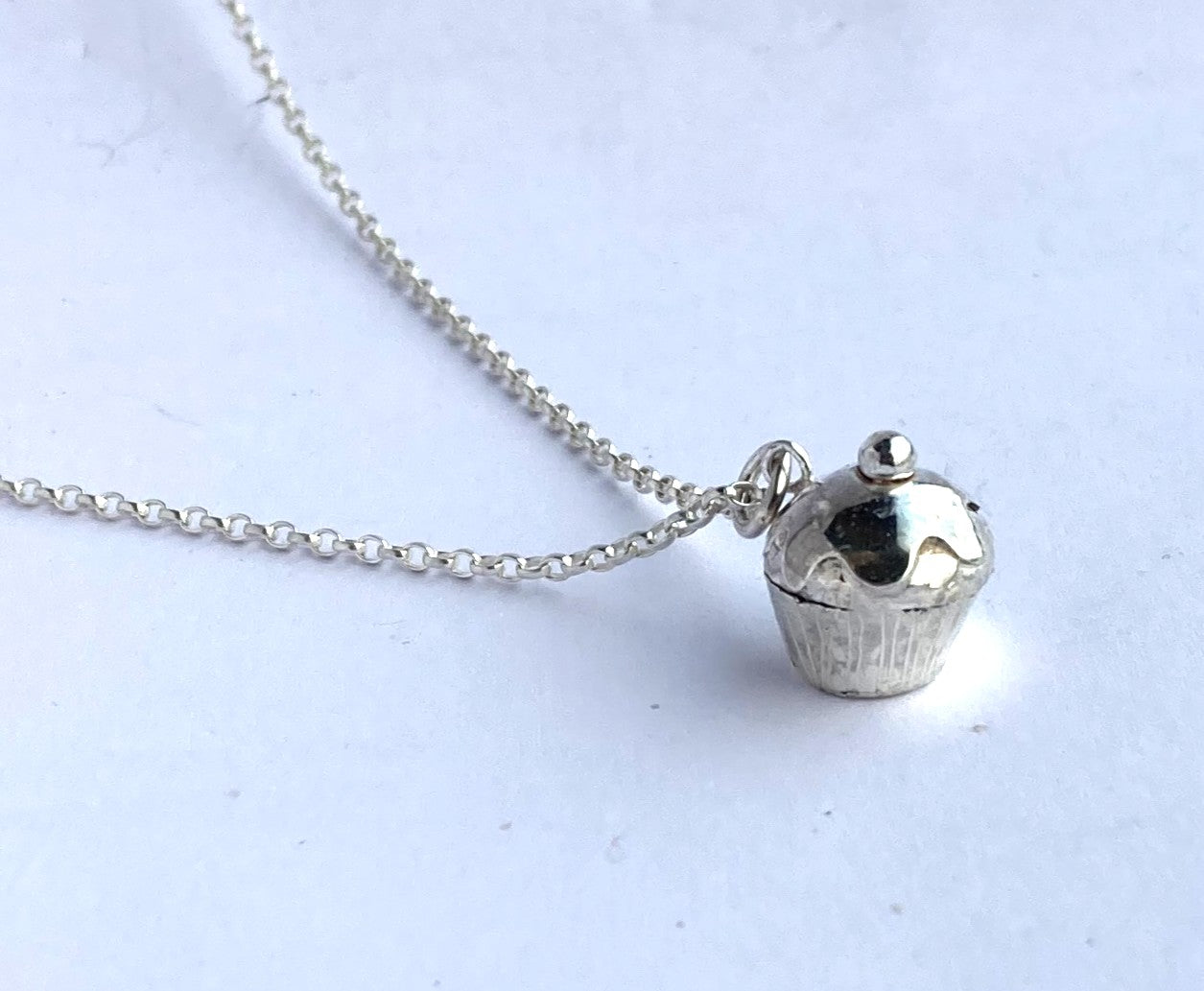 tiny silver cupcake pendant and chain on grey background