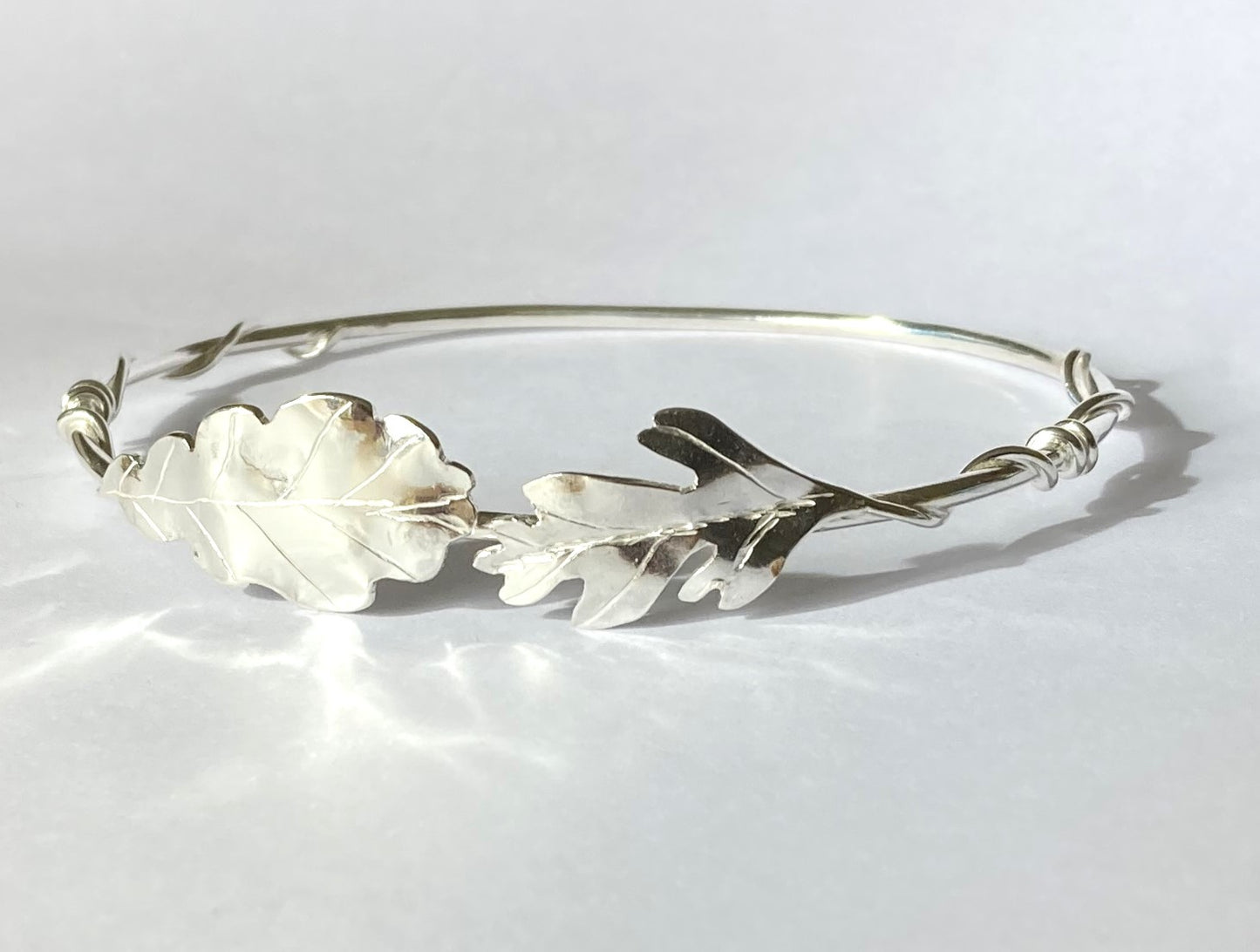 Silver handmade bangle with oak and Hawthorne leaves by Kim Styles Jewellery, on grey background