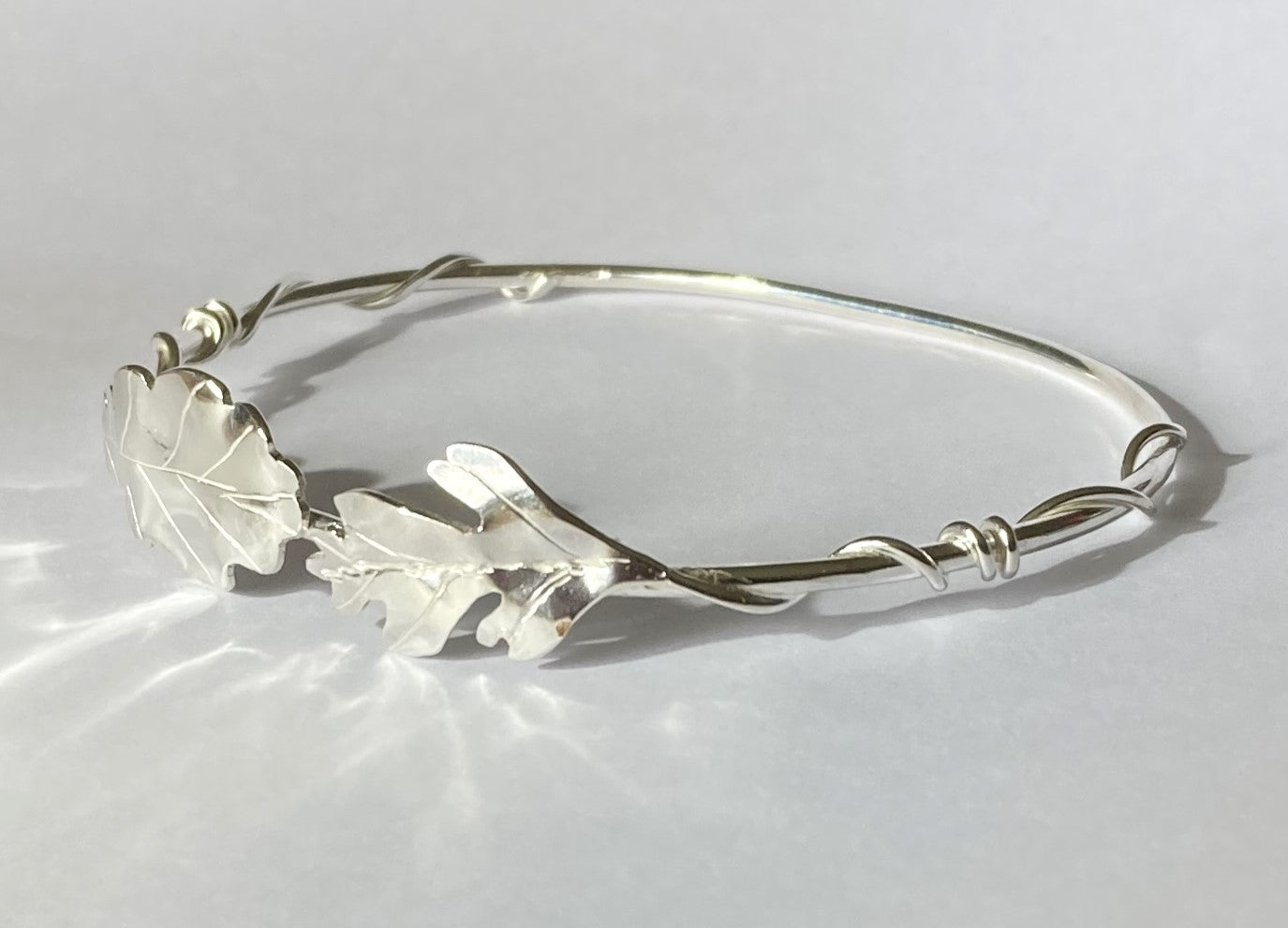 bangle with oak and hawthorn leaves and curly stems, handmade in sterling silver by Kim Styles Jewellery, on grey background