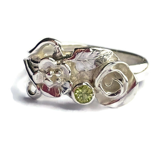 floral silver ring with rosebuds and leaves set with a round green peridot, on white background