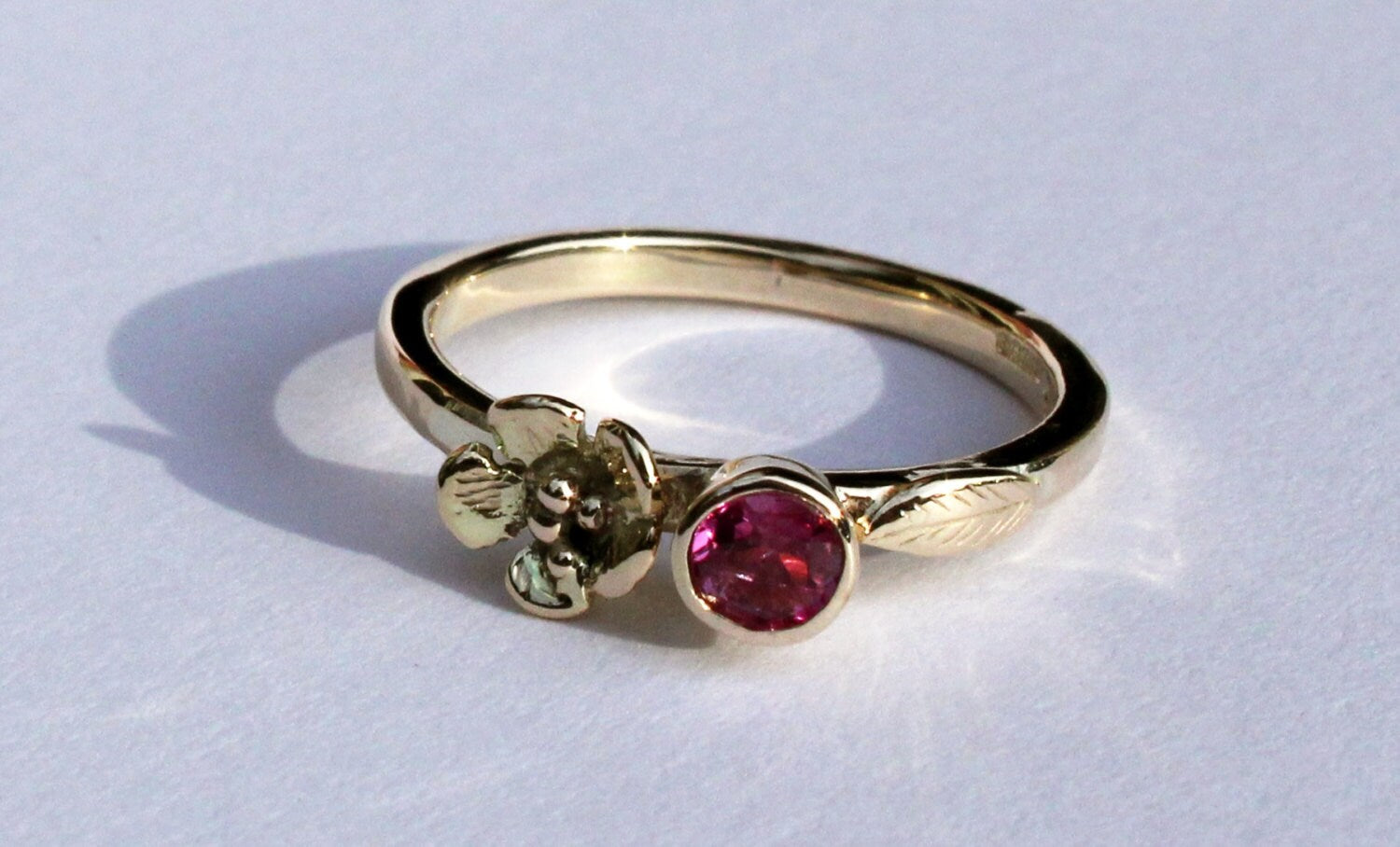 pretty floral yellow gold solitaire engagement ring with bright pink round gemstone, on grey background