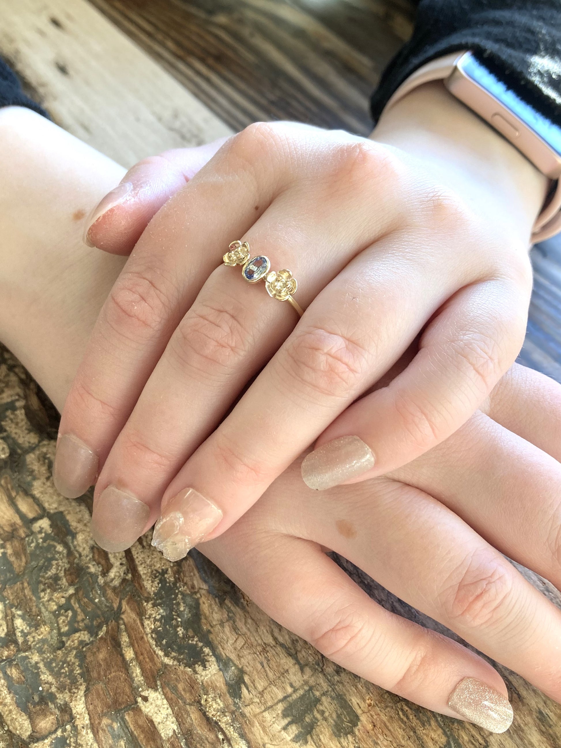 ring with pale blue oval sapphire set in gold with gold flower either side, worn on hand