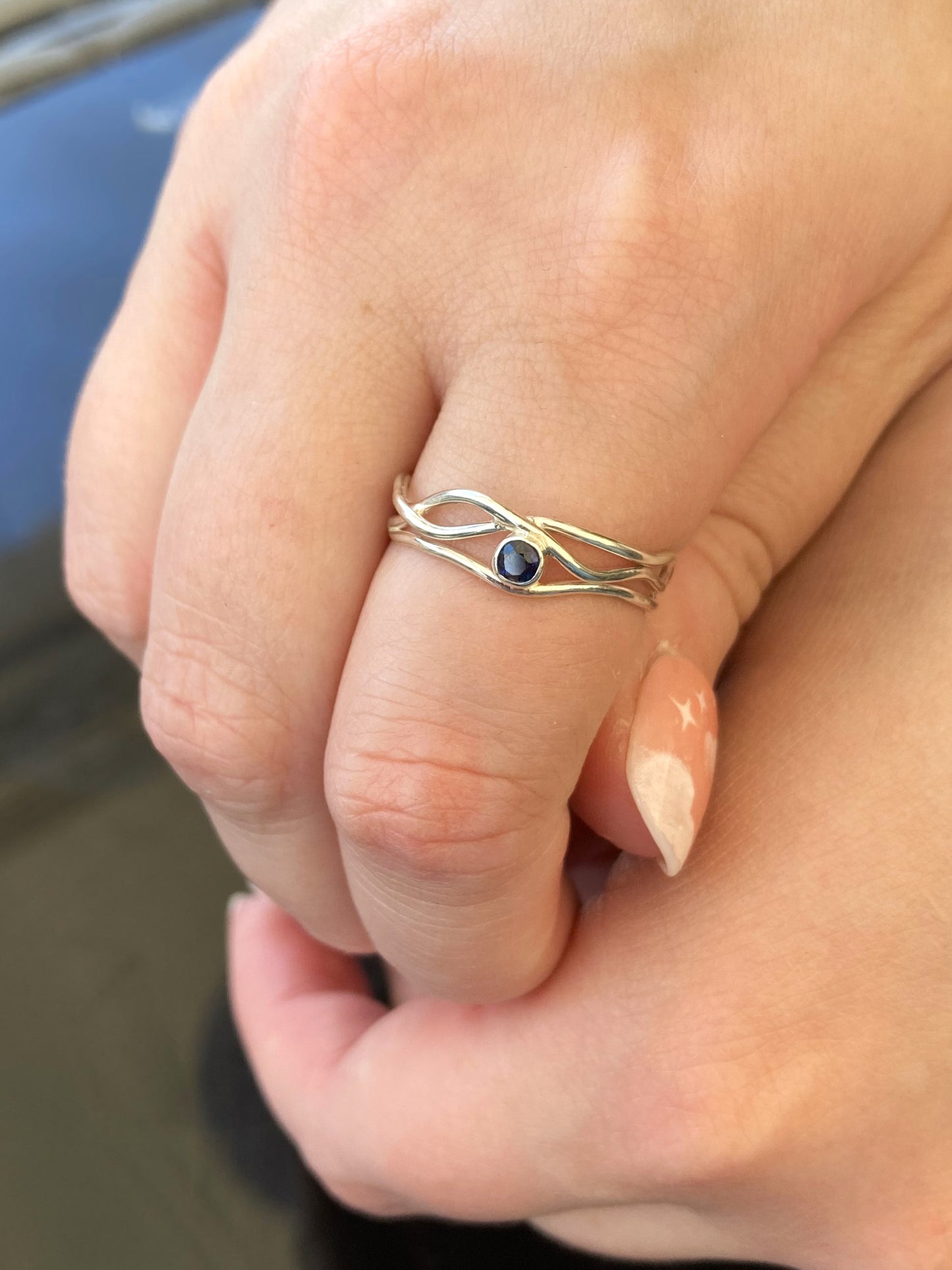 dainty silver wire ring set with blue sapphire, worn on hand