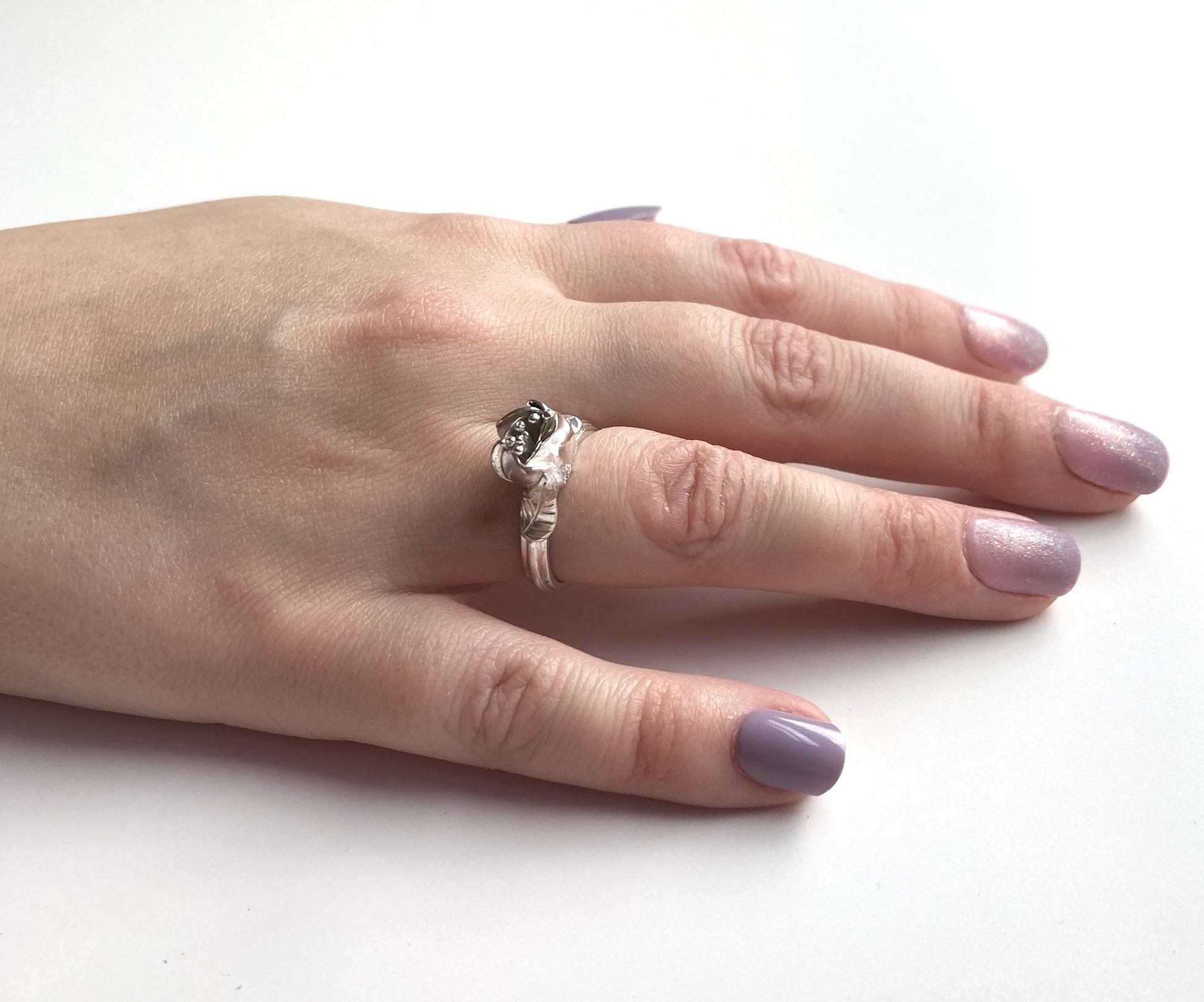 hand with purple nail varnish wearing silver flower bud ring